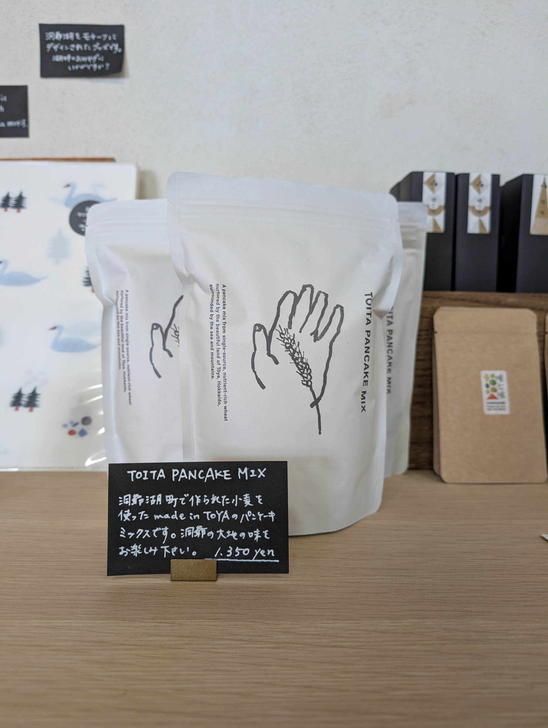 TOITA PANCAKE MIX。白いパッケージに小麦の穂のイラスト。洞爺湖町産の小麦を使ったパンケーキミックス、¥1,350
