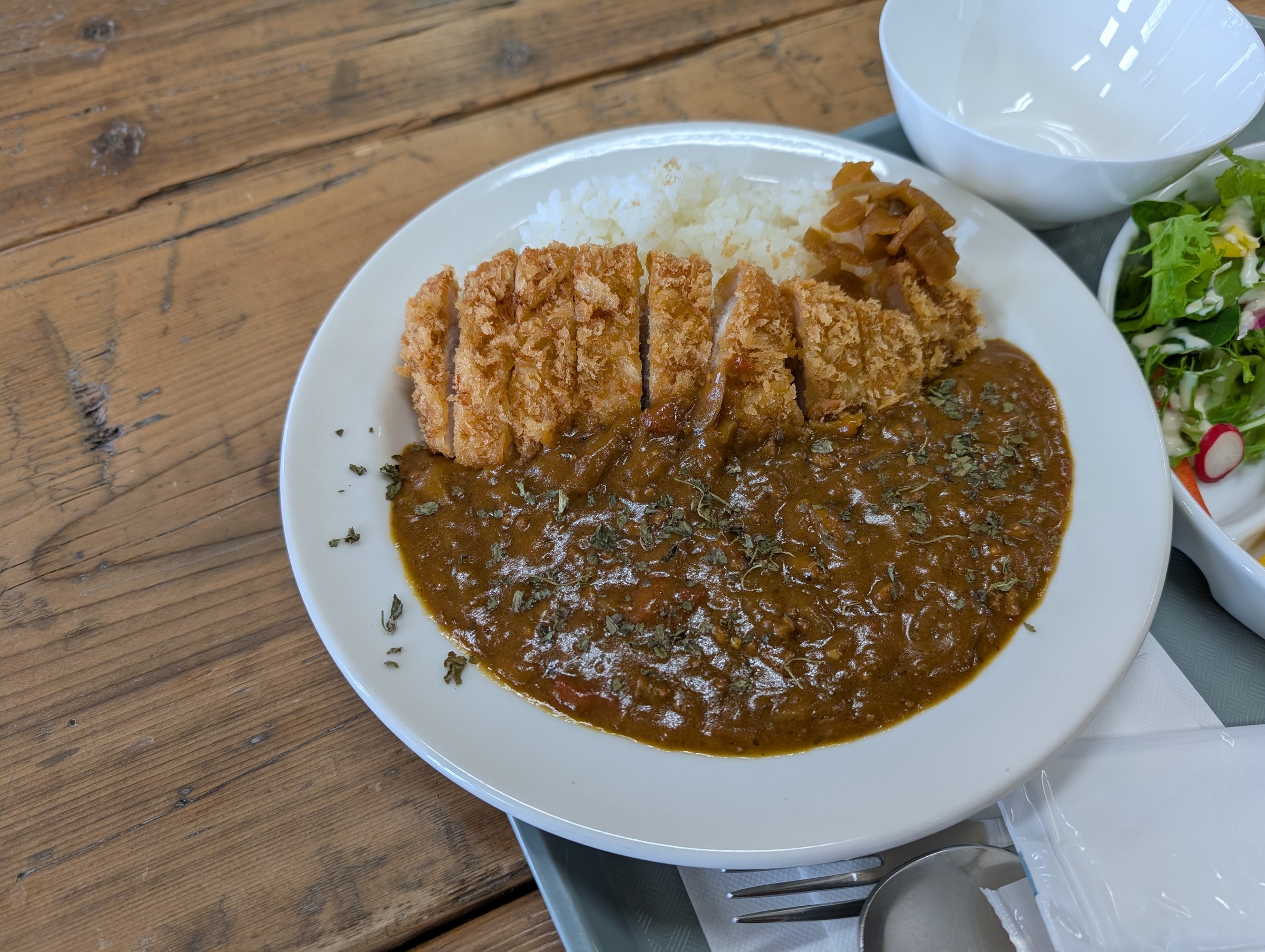 とんかつカレー。厚切りのとんかつがきれいに切り分けられてカレーの上にのっている。サラダと味噌汁が添えられている