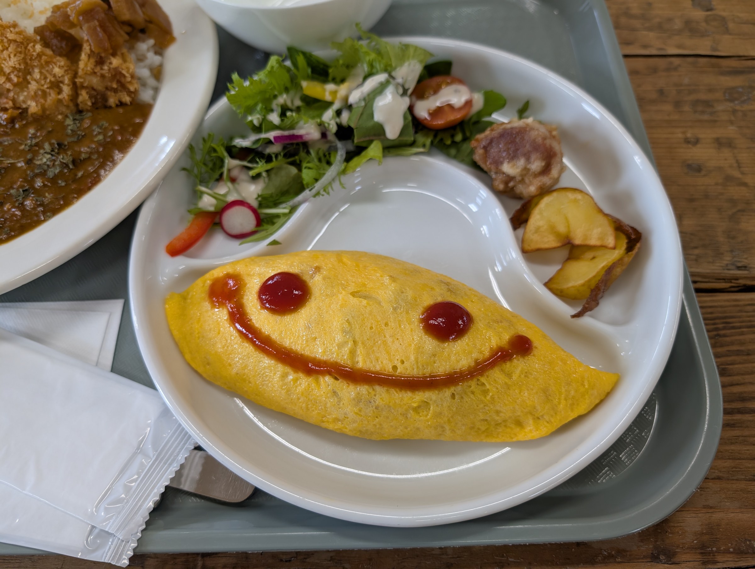 ミニオムライスプレート。ケチャップでにっこりマークが描かれた黄色いオムライスに、サラダとポテトとミートボールが添えられている