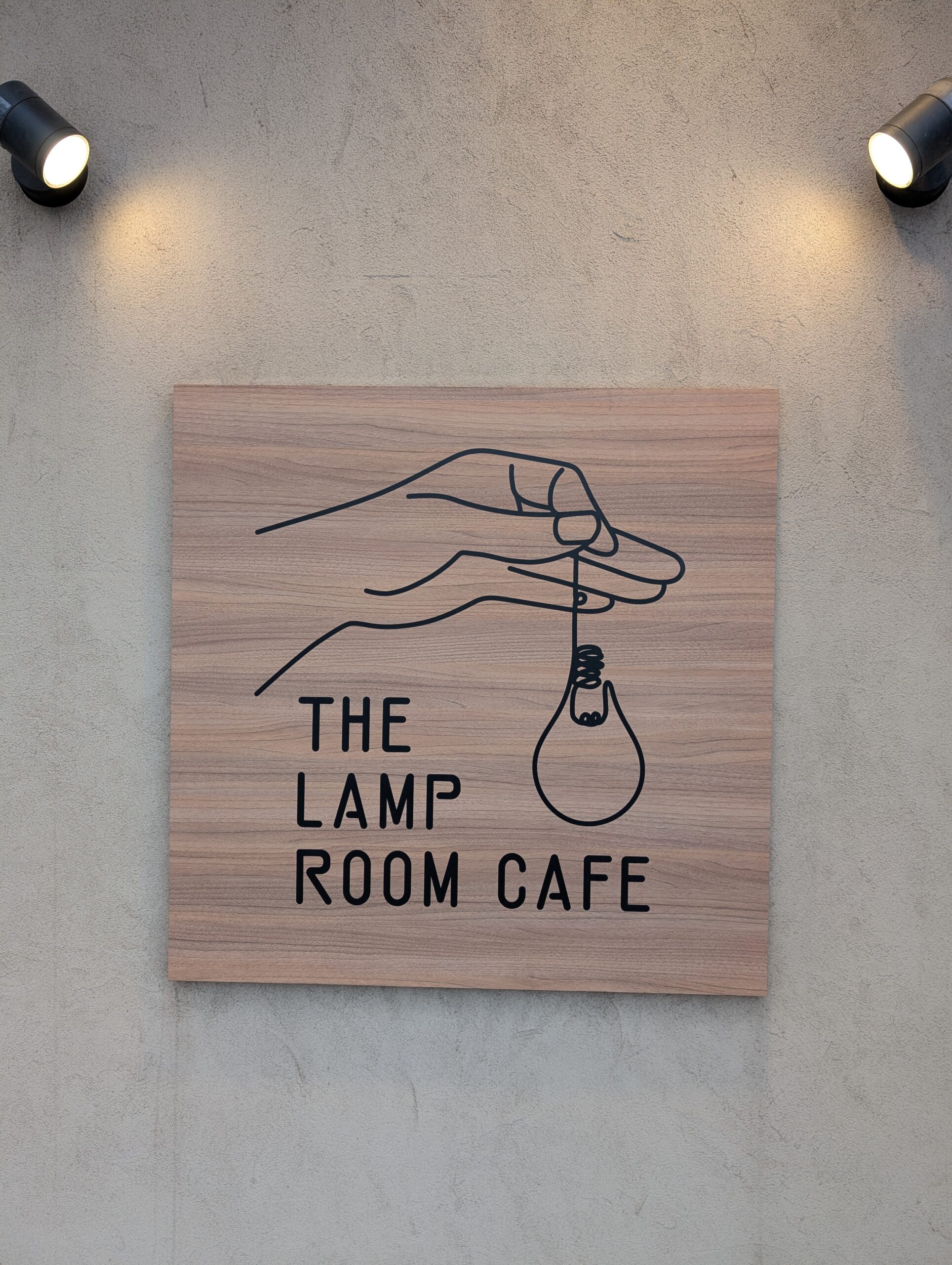 THE LAMP ROOM CAFEのロゴ看板。手が電球を持つイラスト