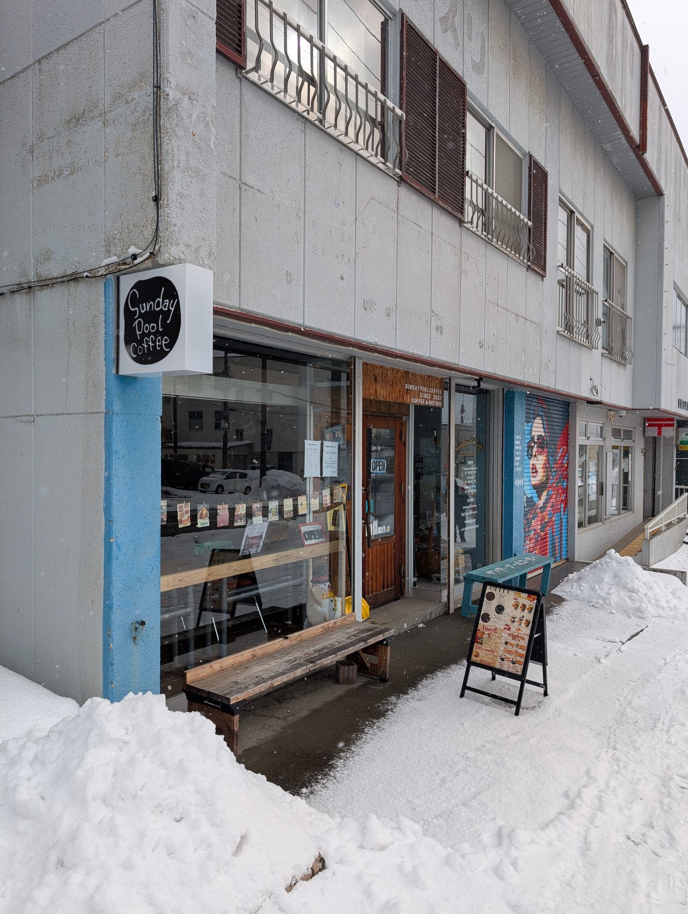 Sunday Pool Coffeeの外観。雪に囲まれたブルーの壁面と木製ベンチ