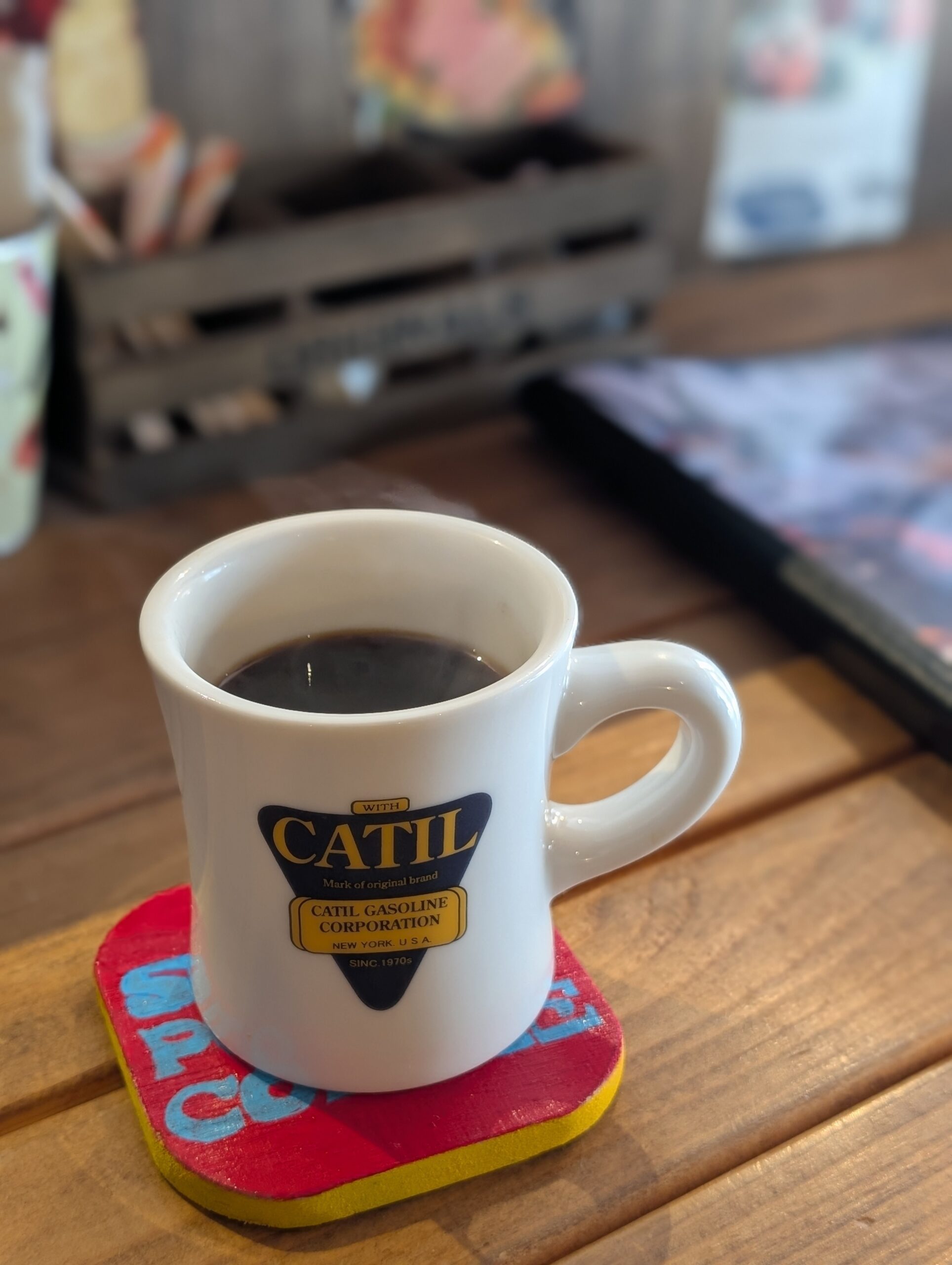 CATILロゴのマグカップに入ったコーヒーとカラフルなコースター