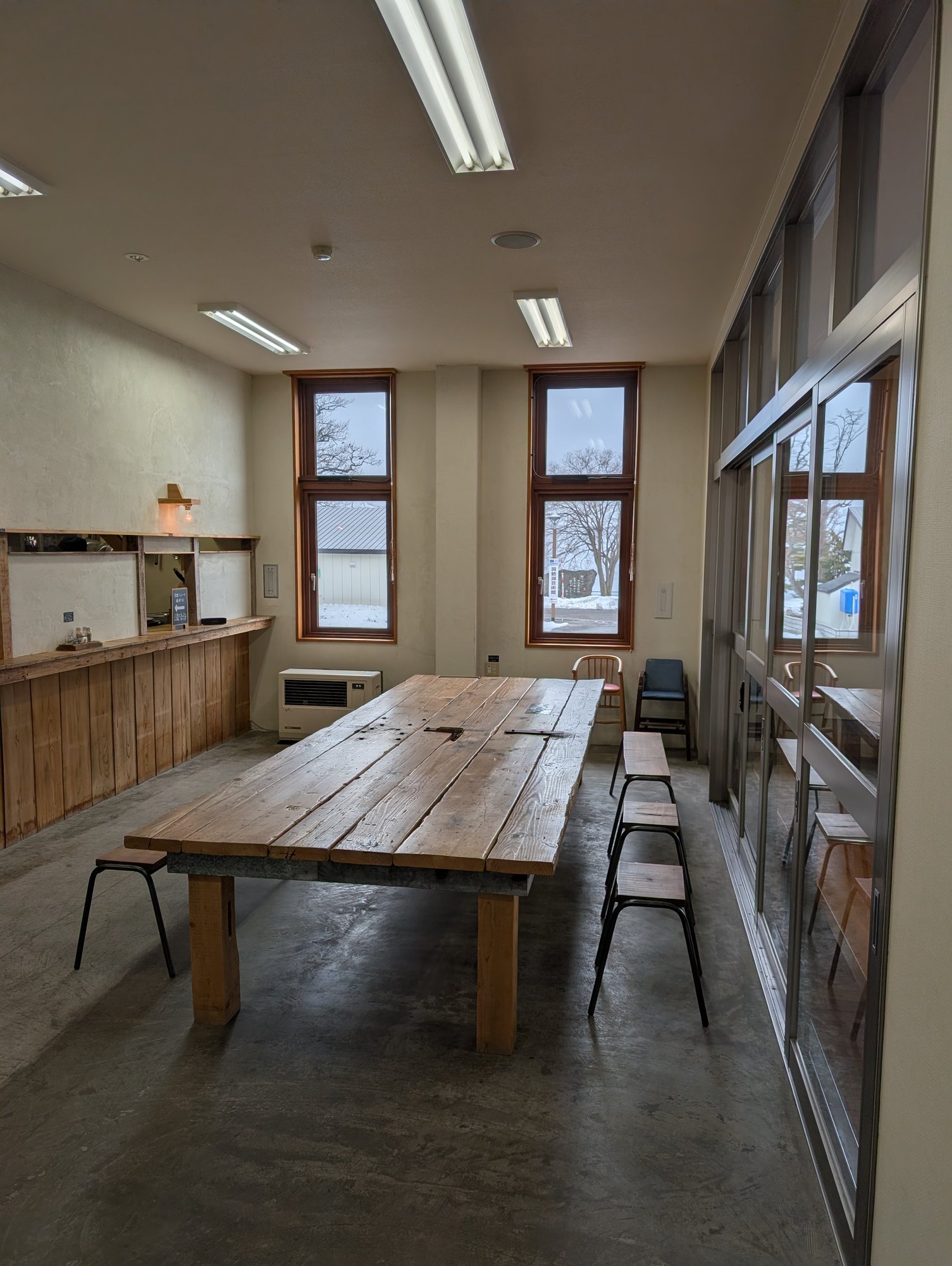 TSUDOUの客席。大きな古材テーブルにスツールが並び、窓から雪景色が見える