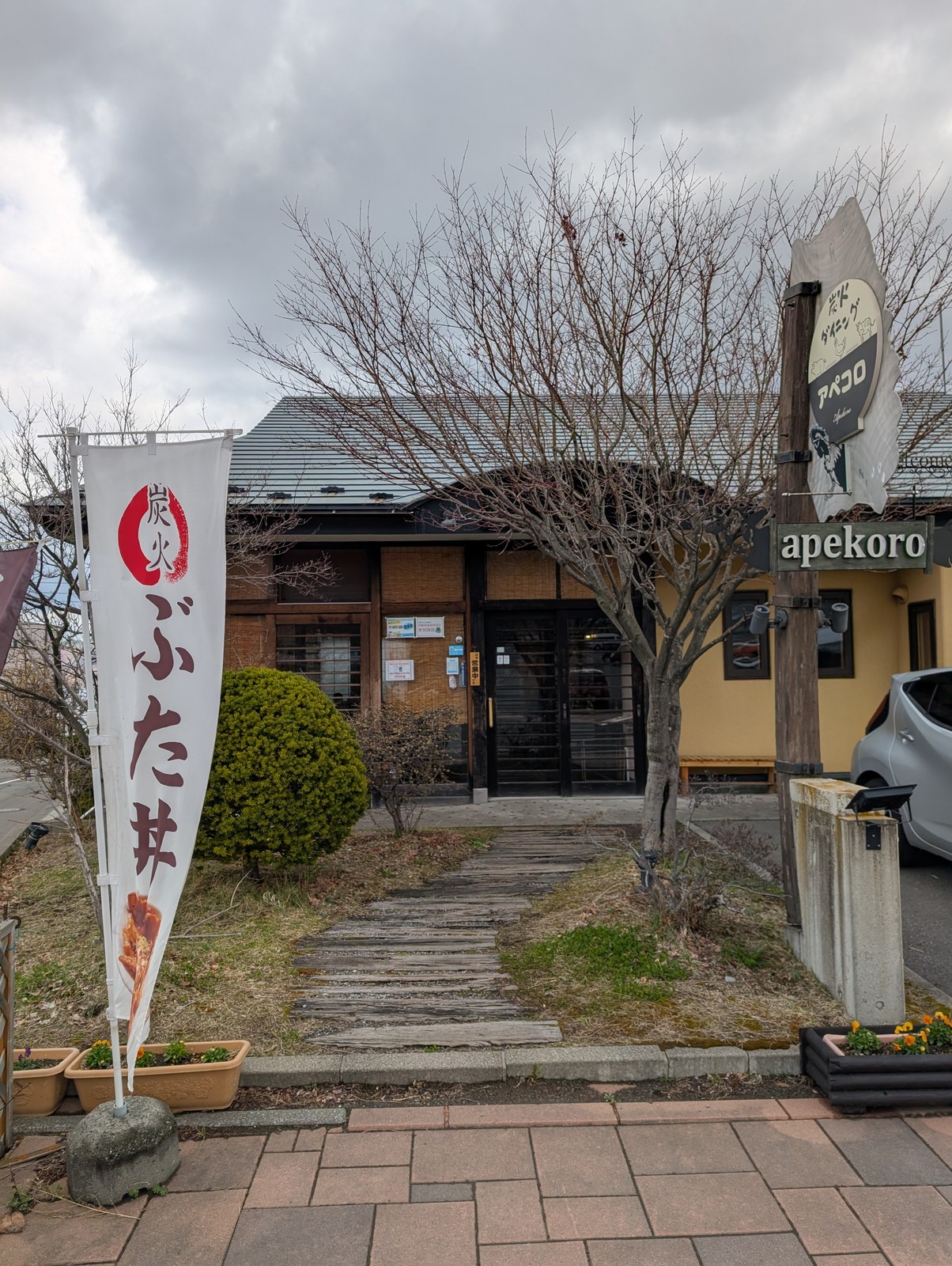 アペコロ外観。石畳の小道の奥にぶた丼の幟とapekoro看板