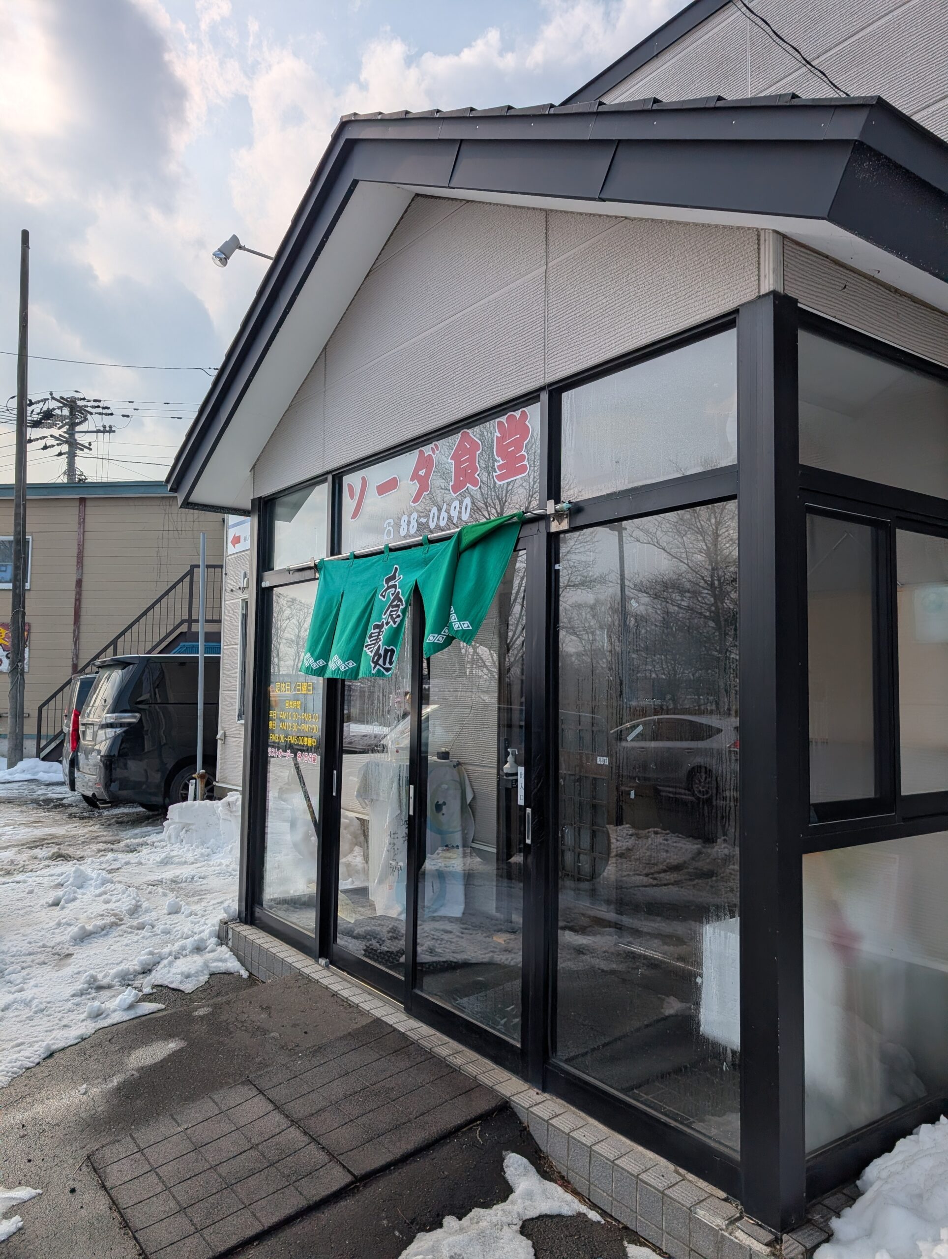 ソーダ食堂の外観。赤い文字の看板と緑の暖簾が目印